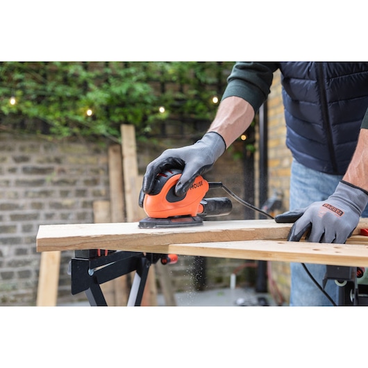 Photography of BLACKDECKER BEW230 mouse sander in use on wooden plank outdoors.