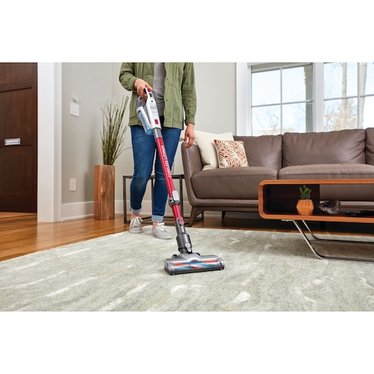 BLACKDECKER BHFE620J cordless stick vacuum in use on a light rug in a modern living room.