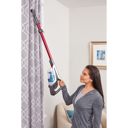 BLACKDECKER BHFE620J cordless stick vacuum with red and silver body cleaning curtains in living room