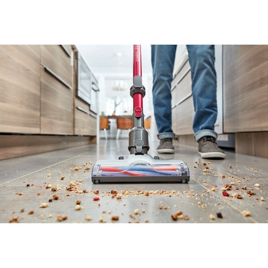 BLACK+DECKER BHFE620J cordless stick vacuum cleaning kitchen floor with debris, low angle close-up.