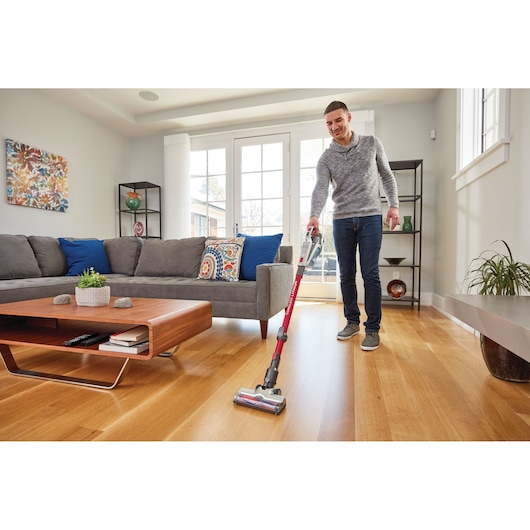 BLACKDECKER BHFE620J cordless stick vacuum cleaner used on hardwood floor in modern living room, side angle.