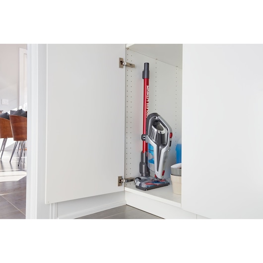 BLACKDECKER BHFE620J cordless stick vacuum cleaner with red and grey design stored upright inside a white cabinet.