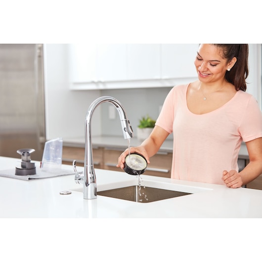 Photo of person rinsing BLACK+DECKER BHFE620J vacuum part under kitchen faucet in modern kitchen.