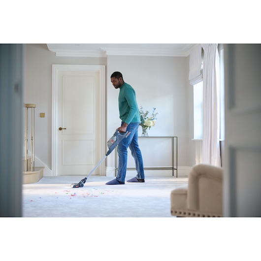 Person using BLACK+DECKER BHFEA18D1 cordless vacuum cleaner on light carpet in modern living room.