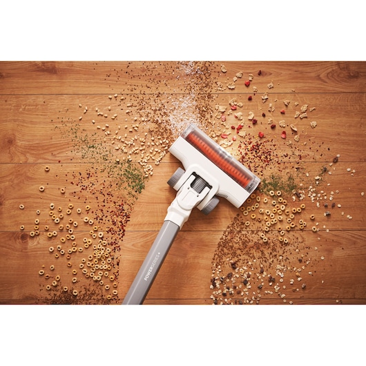 A cordless vacuum cleaner head cleaning assorted dry debris and cereal from a wooden floor.