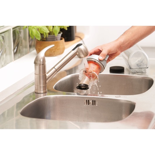 A person rinses a vacuum filter under running water in a kitchen sink with a stainless steel faucet.