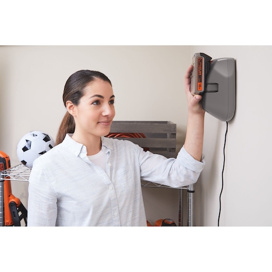 Person placing BLACKDECKER BHFEV182C battery into wall-mounted charger in a garage or storage area.
