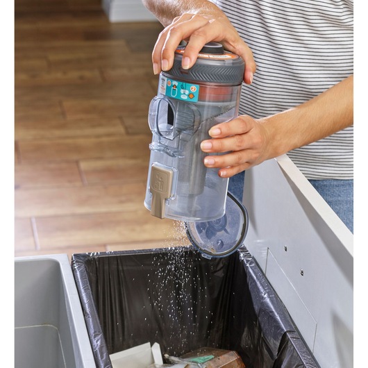 BLACKDECKER BHFEV36B2D vacuum dust container being emptied into trash bin, close-up photography.