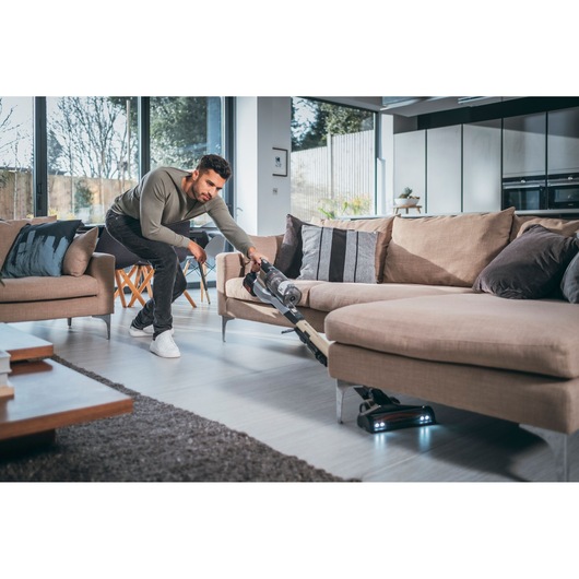 BLACKDECKER BHFEV36B2D cordless vacuum cleaner cleaning under beige sofa in modern living room.