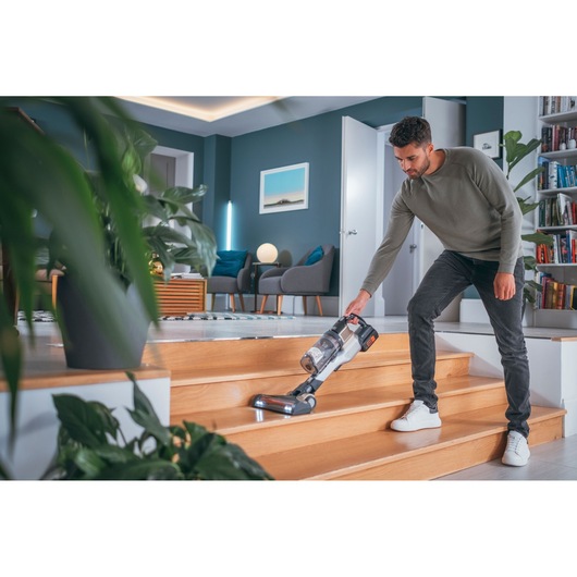 Photo of person cleaning wooden stairs with BLACK+DECKER cordless vacuum BHFEV36B2D in modern living room.