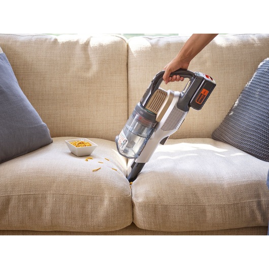 Photo of BLACK+DECKER BHFEV36B2D cordless vacuum cleaner being used to clean crumbs from a beige sofa.