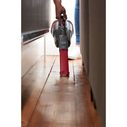 BLACKDECKER BHHV315J handheld vacuum with red nozzle cleaning narrow space on wood floor.