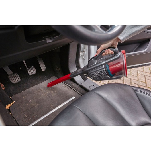 BLACKDECKER BHHV315J handheld vacuum cleaner used to clean car footwell with red extension nozzle.