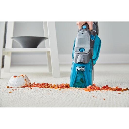 BLACK+DECKER BHSB315J handheld vacuum cleaning spilled food from a light carpet, front angle.