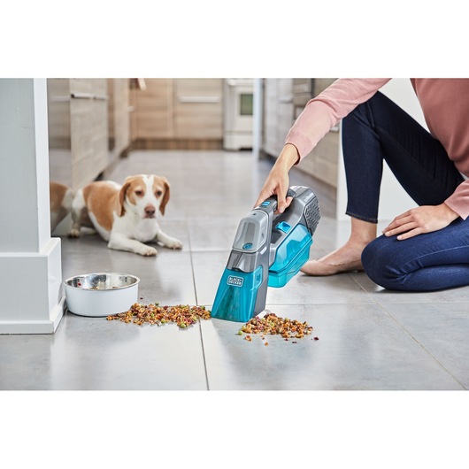 BLACKDECKER BHSB315J handheld vacuum cleaning pet food from tile floor near dog and bowl, side angle.