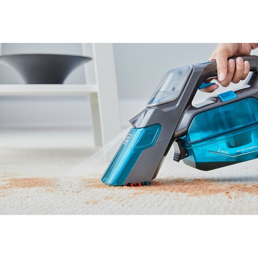 BLACKDECKER BHSB315J handheld carpet cleaner spraying and scrubbing a stain on carpet, side angle.