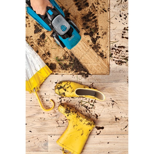 BLACKDECKER BHSB320JP handheld vacuum cleaning muddy entry mat, yellow boots and umbrella on wood floor.