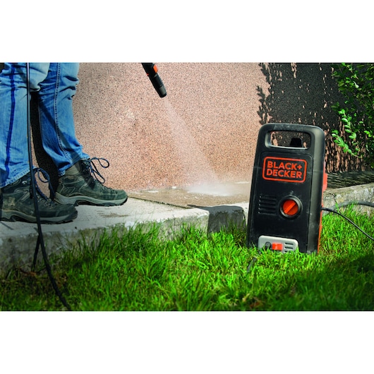 BLACK+DECKER BXPW1300E pressure washer cleaning concrete outdoors, person holding spray wand.
