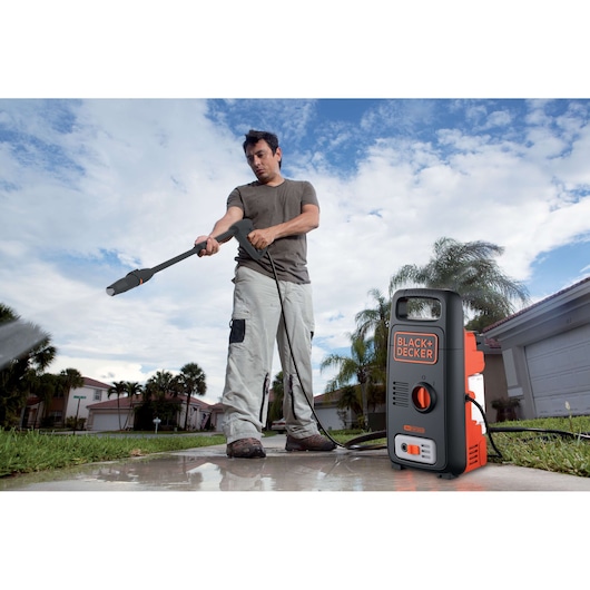 BLACKDECKER BXPW1300E pressure washer on sidewalk, shown in use outdoors near homes and palm trees.