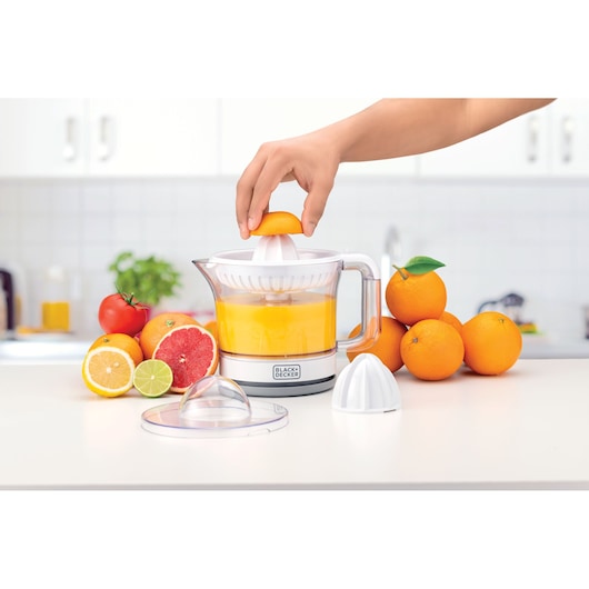BLACK+DECKER CJ675 citrus juicer in kitchen, juicing oranges, surrounded by fresh citrus fruits.