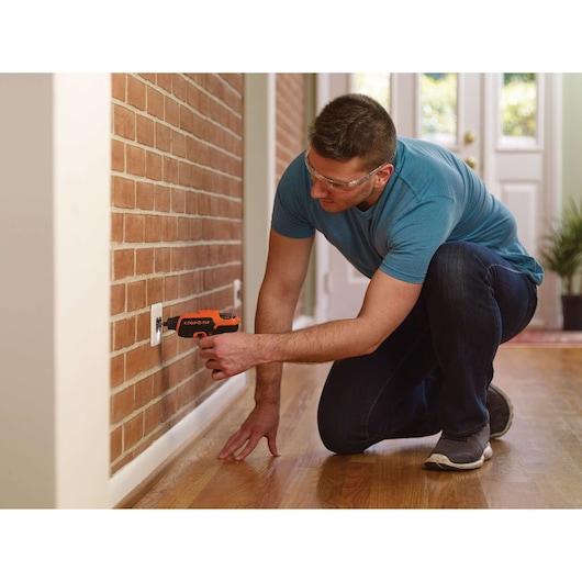 BLACK+DECKER CS36BSCROTO screwdriver used to install an outlet cover on a brick wall in a modern home interior.