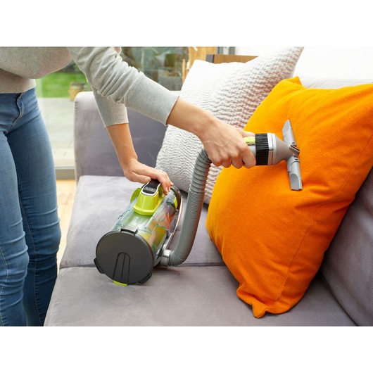 BLACKDECKER CUA525BHA handheld vacuum cleaning orange pillow on grey sofa, close-up, home setting.