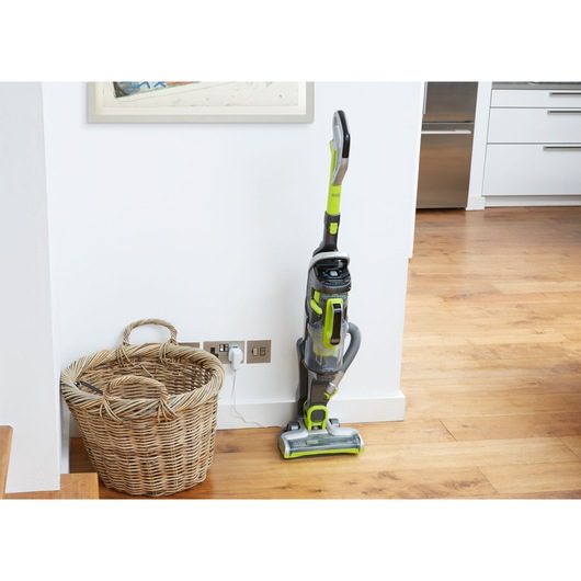 BLACKDECKER CUA525BHA upright vacuum cleaner with green accents, standing beside wicker basket in home interior.