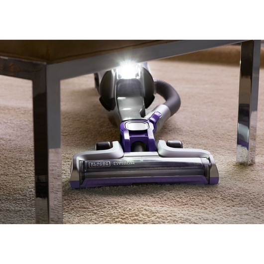 BLACKDECKER CUA525BHP cordless vacuum with LED light cleaning under furniture on carpet, front angle.
