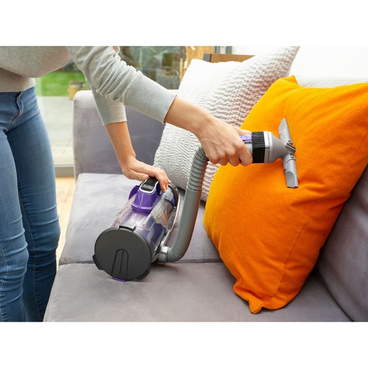BLACKDECKER CUA525BHP handheld vacuum cleaner with hose cleaning orange cushion on grey sofa.