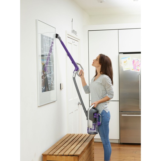BLACKDECKER CUA525BHP vacuum cleaner with purple extension being used to clean a wall frame in a modern kitchen.