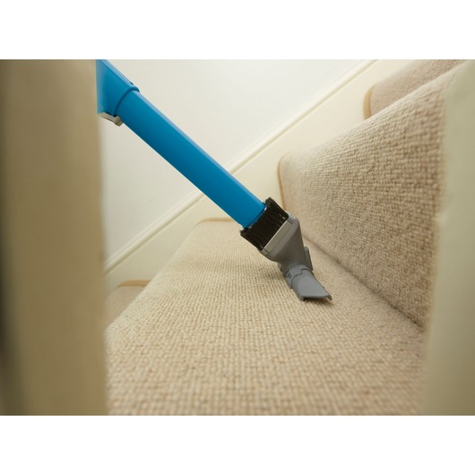 BLACKDECKER CUA525BH vacuum cleaning beige carpeted stairs, close-up of nozzle brushing step.
