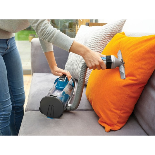 BLACKDECKER CUA525BH handheld vacuum cleaning an orange cushion on a sofa.