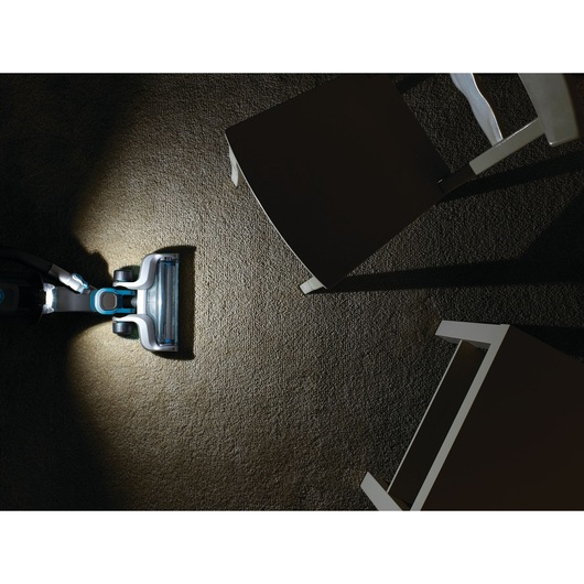 BLACKDECKER CUA525BH vacuum cleaner head with LED light cleaning carpet under chairs, top view.
