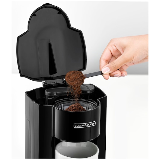 BLACKDECKER DCM25N coffee maker front view with ground coffee being added to filter above white mug.