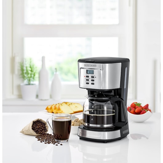 BLACKDECKER DCM85 coffee maker front angle with glass carafe beside coffee cup, beans, bread, and strawberries.