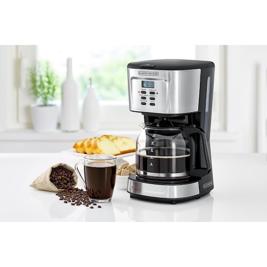 BLACKDECKER DCM85 coffee maker with glass carafe on kitchen counter, cup of coffee and beans beside it.