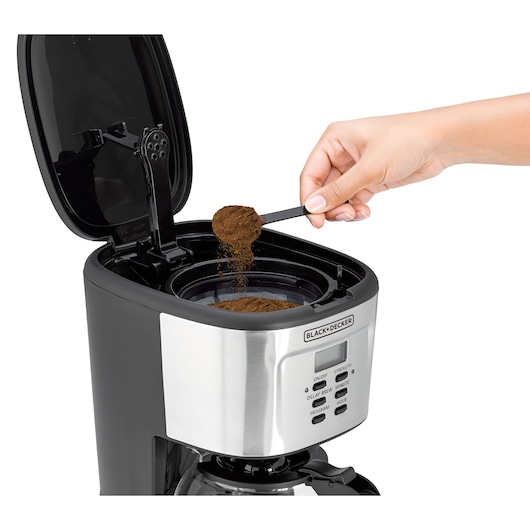 BLACK+DECKER DCM85 coffee maker front angle with open lid, hand adding ground coffee using a scoop.