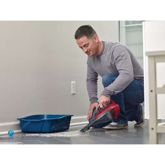 BLACKDECKER DVA315J hand vacuum cleaning floor near blue litter box, side angle.