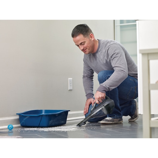 BLACKDECKER DVA320J handheld vacuum cleaning litter near blue tray on tile floor, indoor scene.