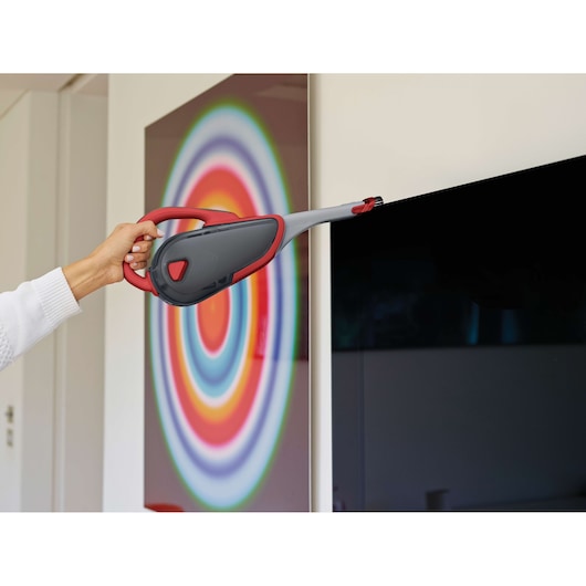 Photo of BLACKDECKER DVJ315J handheld vacuum cleaner with red and gray design cleaning a television screen.