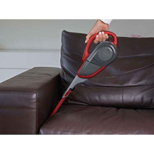 BLACKDECKER DVJ315J handheld vacuum cleaner with red accents cleaning a brown leather sofa.