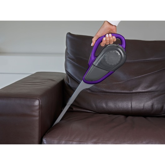 BLACKDECKER DVJ325BFSP handheld vacuum with purple accents cleaning brown leather sofa.