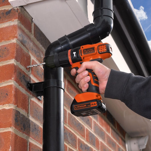 BLACKDECKER EGBL148KB cordless drill being used to drill into exterior brick wall, close-up side angle.