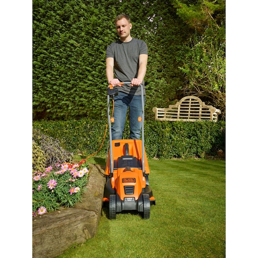 Photo of BLACKDECKER EMAX32S electric lawn mower in use on grass near flower bed.