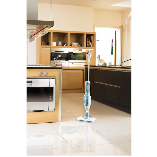 A BLACK+DECKER steam mop (model FSM1630) is standing on a tiled kitchen floor, surrounded by modern kitchen cabinets and appliances.