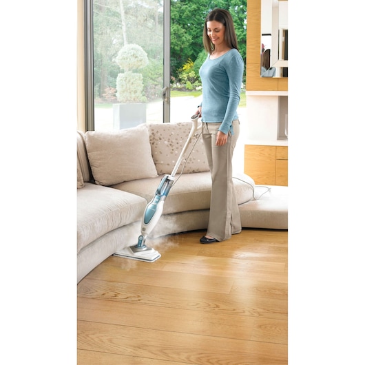 BLACKDECKER FSM1630 steam mop in use on hardwood floor near sofa, releasing visible steam.