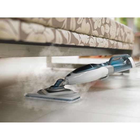 BLACKDECKER FSM1630 steam mop cleaning tile floor under a floral fabric sofa, handheld angle.