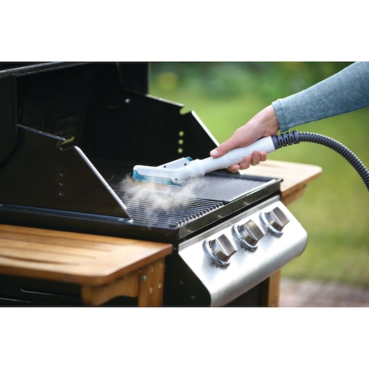 A person uses a steam cleaning tool to clean the grill grates of an outdoor barbecue grill.