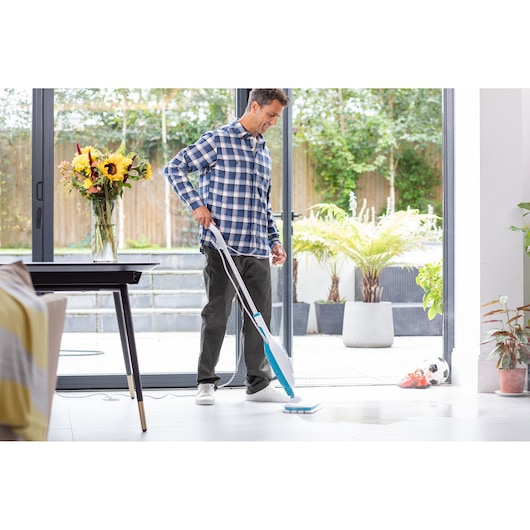 BLACKDECKER FSMH13E5 steam mop cleaning white tile floor near open glass doors, flowers on table, indoor plants.