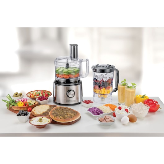 BLACK+DECKER FX760SB food processor and blender on a white surface with assorted vegetables, fruits, and dishes, front view.
